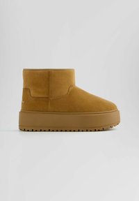 Tan suede ankle boots with a flat, ridged sole and minimalistic design. Features a stitched seam detail and a raised heel section.