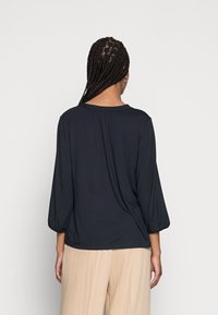 Blouse bleu marine foncé avec une coupe décontractée, manches bouffantes trois-quarts et un léger froncé au niveau de l'encolure dans le dos. Tissu doux et léger.