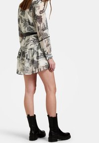 Krátké, průhledné šaty s černobílým tropickým vzorem; rýhovaný lem a rukávy. Spárováno s černými kotníkovými botami s robustní podrážkou.