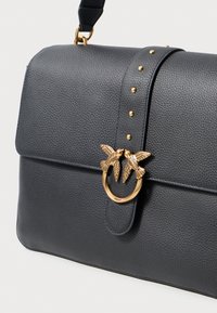 Bolsa de couro cinza escuro estruturada, com fecho de cordão dourado decorado com detalhes de pássaros, tachas douradas na alça e um acabamento texturizado.