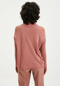Rosa oversized sweater med ribbet tekstur og åben skulderdesign, parret med matchende bukser. Blødt strikstof.