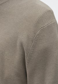 Grå striktrøje med tekstureret, ribstrikket stof og en afslappet pasform. Halsudskæringen er rund med faldende skuldre og diskrete syningsdetaljer.