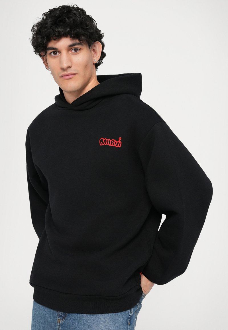 Svart huva med en röd broderad logotyp på bröstet. Gjord av mjukt tyg med en avslappnad passform och ribbade ärmslut.