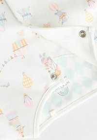Tutina crema con motivi a palloncini e animali in tonalità pastello, dotata di chiusure a scatto e realizzata in morbido cotone. Caratteristico accento a quadri in azzurro chiaro.