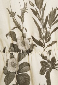 Tessuto a fiori nei toni beige e verde scuro, con grandi fiori, foglie e un dettaglio di cucitura arricciata in vita.