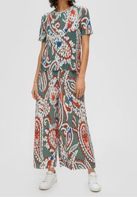 Femme portant un haut à manches courtes assorti et un pantalon large avec un motif floral abstrait vert, rouge, blanc et bleu, associé à des baskets blanches.