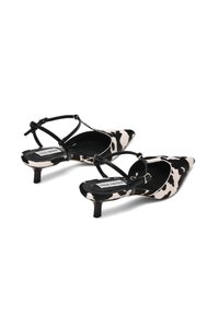 Scarpe con tacco a punta in tessuto a stampa mucca bianca e nera. Presentano un tacco sottile e una progettazione a cinturino incrociato per una vestibilità sicura.