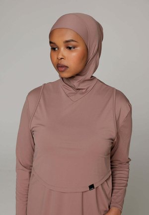 Vrouw draagt een mauve langärmelig sporttopje met bijpassende aansluitende hijab, kijkt naar beneden en opzij tegen een effen achtergrond.