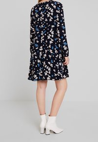Blommig klänning i marinblått med vita och blå blommor, långa ärmar och en utsvängd siluett. Matchad med vita ankelstövlar.