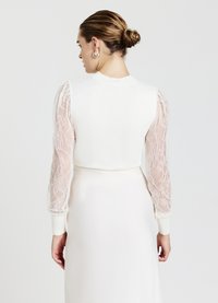 Weißes gestricktes Top mit transparenten Spitze-Puffärmeln, featuring einen runden Halsausschnitt und gerippten Bündchen. Glattes Material in einer taillierten Form.