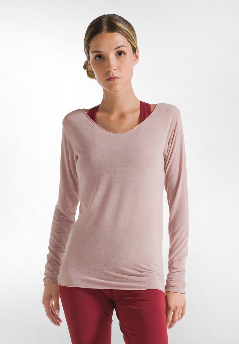 Hellrosa Langarmshirt mit weitem Ausschnitt und gerafftem Detail am Saum, über einem bordeauxfarbenen Sport-BH getragen. Weicher, leichter Stoff.