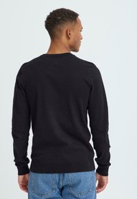 Must päevane must pika varrukaga sviiter ümarate kaelustega, ribivarrukatega ja allservaga, koos helesiniste teksadega. Sile tekstuur, peen disain.