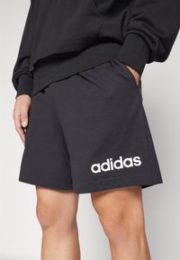 Black cotton athletic shorts featuring an elastic waistband, side pockets, and a white "adidas" logo printed on the lower left side.