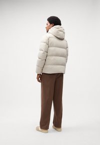 Beige puffer jacket with a hood, featuring a quilted design and a smooth texture. Paired with brown loose-fitting pants and beige sneakers.