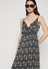 Rochie cu un model alb-negru, cu decolteu adânc în V, bretele subțiri reglabile și o fustă fluidă. Textură de material neted și ușor.