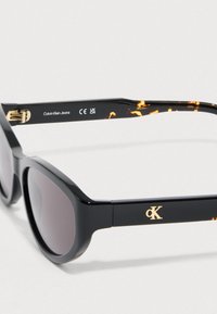 Czarne plastikowe okulary przeciwsłoneczne o błyszczącym wykończeniu, z wzorem w panterkę na zausznikach oraz złotym logo "CK".