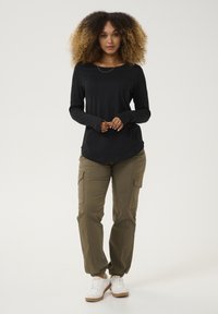 Schwarzes Langarmoberteil mit Rundhalsausschnitt, kombiniert mit olivfarbenen Cargo-Hosen mit elastischen Bündchen und Seitentaschen, abgerundet mit weißen Sneakers.