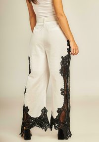 Witte wijde broek met ingewikkelde zwarte kantafwerking aan de zijkanten, gemaakt van een lichtgewicht stof en met een relaxte pasvorm.