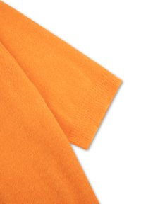 Oranje gebreide stof met een zachte textuur, voorzien van een schuin schoudernaad en een nette rand op de mouw.