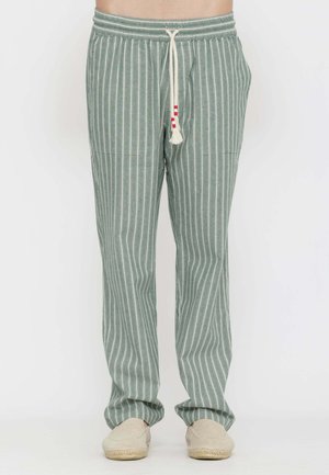 Pantaloni verdi con righe verticali bianche e coulisse bianca, indossati con scarpe slip-on beige chiaro su una persona in piedi.