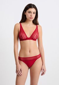 Czerwony zestaw koronkowej bielizny zawierający trójkątny biustonosz z przezroczystego, w paski materiału oraz pasujące majtki typu bikini z koronkowymi akcentami na pasku.