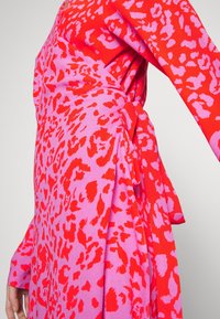 Bunt bedrucktes Wickelkleid mit einem auffälligen roten und rosa Leopardenmuster, langen Ärmeln und einer gebundenen Taille für zusätzliche Details.