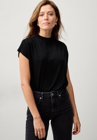 Sort kortærmet skjorte med høj hals, lavet af glat stof. Bæres med mørke denim jeans. Simpelt design uden synlige mønstre.