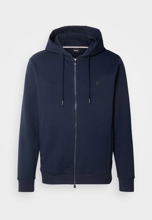 Felpa blu navy con zip, cappuccio regolabile con coulisse, polsini a coste, tasche laterali e un piccolo logo sul petto. Realizzata in tessuto morbido.