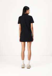 Black polo dress with short sleeves and a collar, featuring a straight cut and a slightly elongated back. No visible patterns or details.