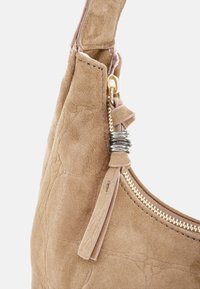 Borsa a tracolla in camoscio color cuoio con cerniera dorata, superficie testurizzata e dettaglio a nappina. Presenta un dettaglio a spirale metallica sulla tracolla.