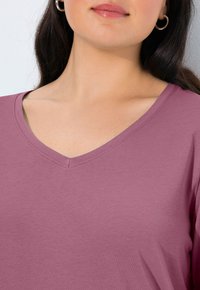 Halenka s výstřihem do V vyrobená z měkké levandulové látky. Má hladkou texturu a volný střih, s přesně sešitými okraji.