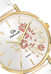 Montre dorée avec un motif floral sur un cadran blanc, index en or et bracelet en cuir blanc. Elle dispose d'un mouvement à quartz.