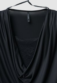 Schwarzes Kleidungsstück mit tiefem V-Ausschnitt, aus glattem Stoff gefertigt. Es hat Spitzenakzente am Ausschnitt und verstellbare Träger oben für eine optimale Passform.