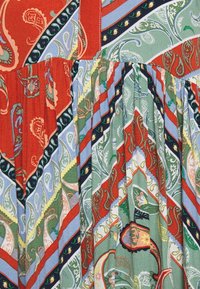 Tissu multicolore avec de complexes motifs paisley en rouge, vert et bleu, présentant des plis verticaux et des accents rayés contrastants.
