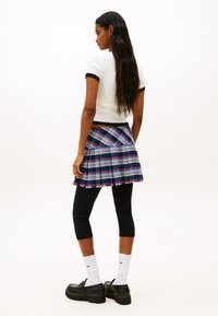 Λευκό τοπ με κοντά μανίκια και μαύρο περίγραμμα, συνδυασμένο με καρώ φούστα σε μπλε, ροζ και λευκό χρώμα και μαύρες κολάν. Βαριά μαύρα παπούτσια και λευκές κάλτσες.