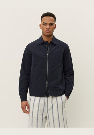 Marineblå hettejakke i lett tekstil med krage, sidelommer og minimalistisk design, parret med stripete, vide bukser.