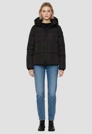 Schwarze gesteppte Jacke mit Kapuze, vorne mit Reißverschluss und zwei Seitentaschen. Getragen über blauen Jeans und schwarzen Stiefeln vor neutralem Hintergrund.