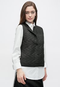 Črna prešita jopica z visokim ovratnikom in zapiranjem na sponke, z značilnim trikotnim vzorcem in gladko, elegantno teksturo.