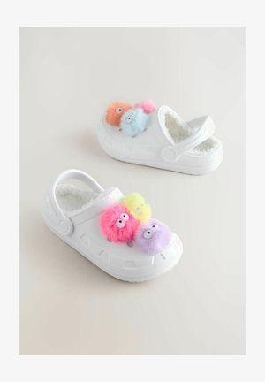 Weiße Clogs mit flauschigen Pom-Pom-Verzierungen in Pink, Lila, Gelb und Blau. Sie verfügen über ein weiches Innenfutter und einen hinteren Riemen für zusätzliche Stabilität.