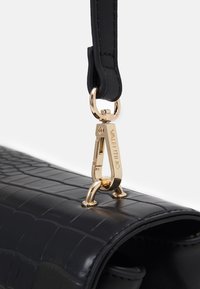 Borsa a tracolla in pelle nera con texture a coccodrillo, dotata di una clip in metallo dorato e del nome del marchio inciso "Valentino."