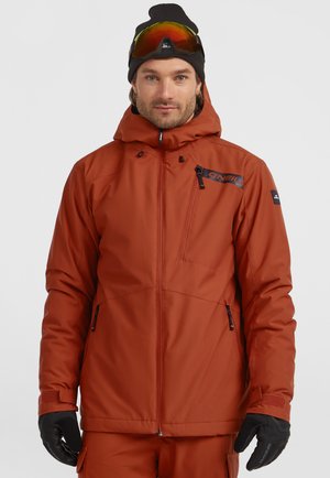 Oranje geïsoleerde skijas met een capuchon, ritszakken en zwarte accenten. Gekocht met zwarte handschoenen en een zwarte muts, voorzien van beschermende goggles.