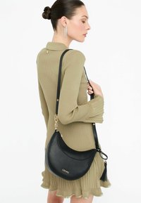 Borsa a spalla in pelle nera con forma a mezzaluna, accessori in oro e dettaglio con nappina. Texture liscia e logo del marchio in rilievo.