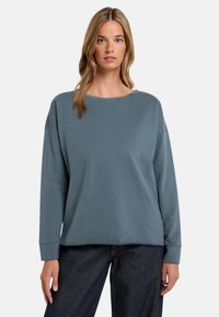 Hellblaues, übergroßes Sweatshirt mit rundem Ausschnitt, überschnittenen Schultern und langen Ärmeln. Weicher Stoff mit glatter Textur.