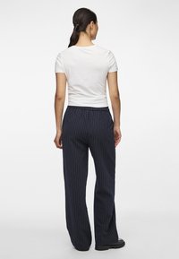 Weißes T-Shirt mit kurzen Ärmeln, kombiniert mit navyblauen, gestreiften Schlaghosen. Die Hosen haben einen elastischen Bund und eine lockere Passform.