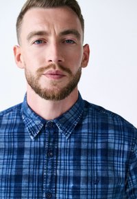 Blau karierte Baumwollbluse mit einem Button-Down-Kragen, vorderen Knöpfen und einem kleinen gestickten Logo auf der Brust.