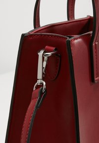 Punainen nahkainen käsilaukku, jolla on jämäkkä muoto, ja siinä on kontrastina musta reuna, hopeiset yksityiskohdat sekä irrotettava hihna.