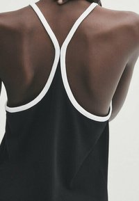 Mustapaita, jossa on urheilullinen selkädesign ja valkoiset reunukset olkaimissa. Kangas näyttää sileältä ja kevyeltä.