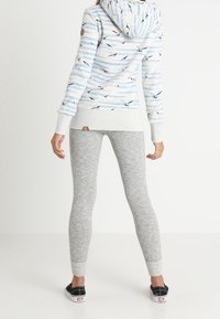 Sudadera con capucha de base gris claro, con un patrón de azul y pájaros; leggings grises de ajuste ceñido, combinados con zapatillas negras.