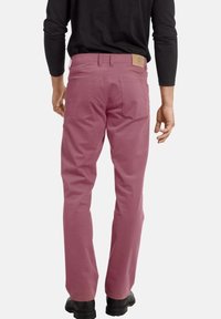 Roze katoenen broek met een ontwerp met rechte pijpen, achterzakken en een leren patch op de tailleband. Draagt bij een zwart shirt met lange mouwen.