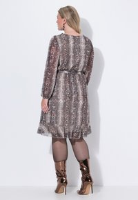 Ein knielanges Kleid mit Schlangenprint in Brauntönen, langen Ärmeln und einem taillierten Bund. Akzentuiert mit glänzenden, knielangen bronzefarbenen Stiefeln.